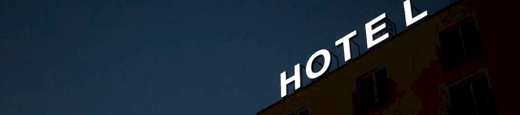 The image shows the side of a building at night with an illuminated sign reading "HOTEL" against a dark sky.