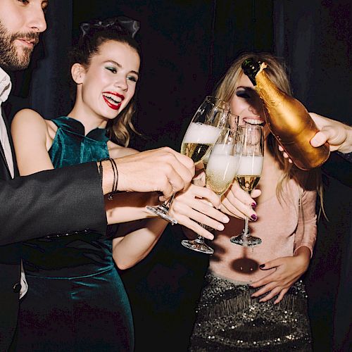A group of friends toasting with champagne flutes at a party, dressed stylishly and smiling as drinks are poured.