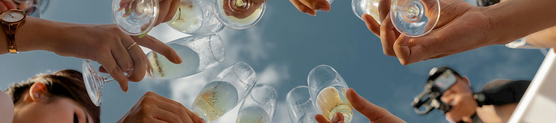 A group cheers with tiny glasses in a sunny outdoor setting, clinking drinks together as they toast one another.