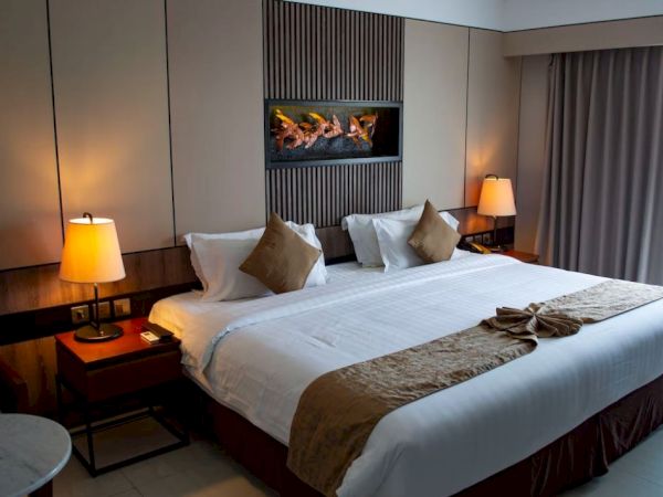 A neatly made bed with pillows, lamps on side tables, and a decorative wall piece in a cozy, softly lit room with curtains.