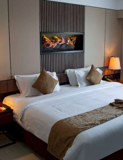 A well-lit hotel room with a large bed, decorative pillows, bedside lamps, and a window with curtains. A stylish and cozy ambiance.
