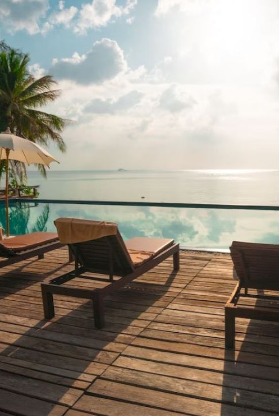 A serene tropical setting with lounge chairs, umbrellas, and a calm pool overlooking the ocean and sky.
