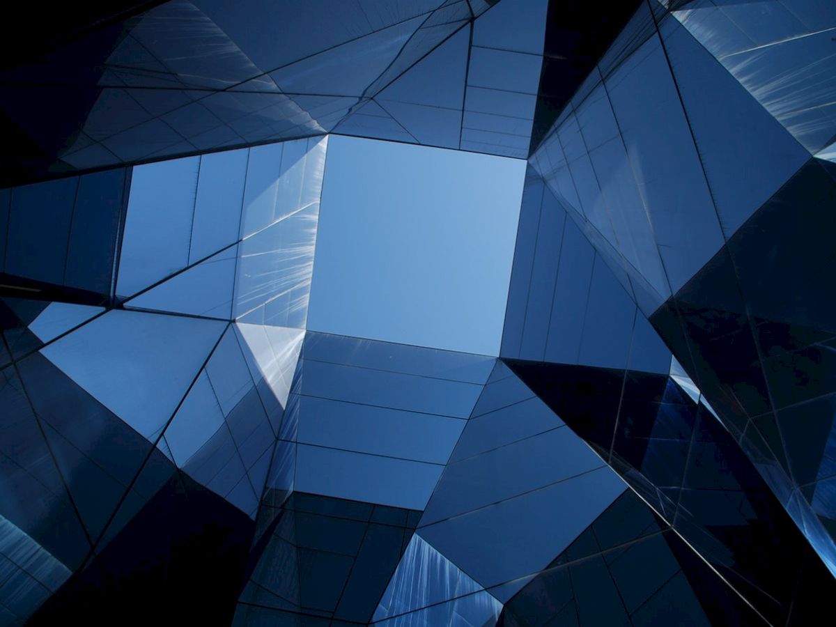 The image shows a geometric architectural structure with mirrored surfaces reflecting a blue sky, creating an abstract visual effect.