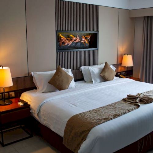A cozy hotel room with a large bed, warm lighting, a decorative piece above the bed, and two side tables with lamps.
