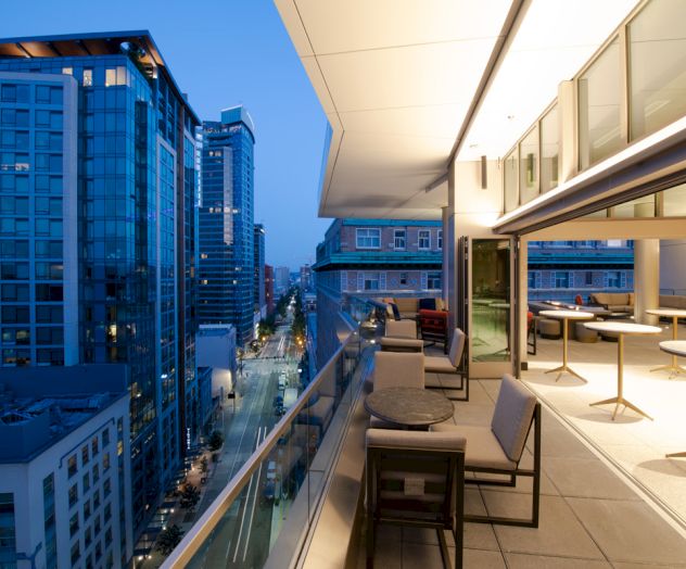 A modern rooftop terrace with seating overlooks a cityscape and tall buildings, captured at dusk with ambient lighting.