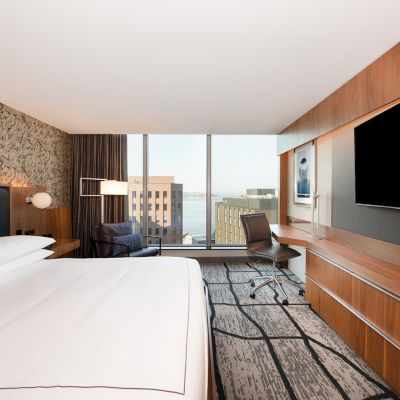 A modern hotel room features a large bed, wall-mounted TV, desk, and window with a cityscape view, combining comfort and style.