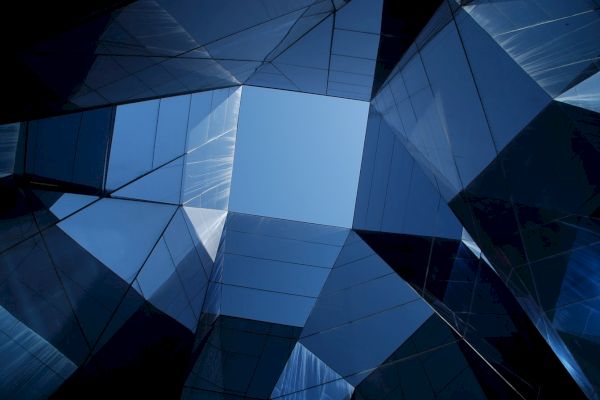 A view of the sky framed by tall, reflective glass buildings, creating a geometric and symmetrical architectural scene.