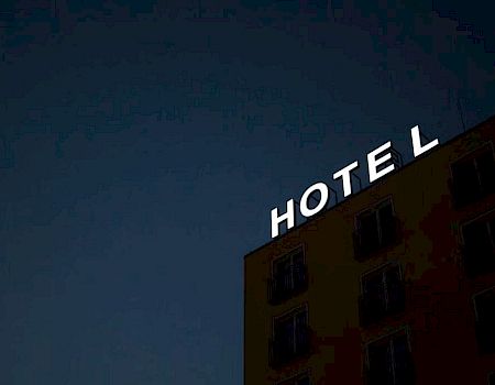 The image shows the side of a building at night with an illuminated sign reading "HOTEL" against a dark sky.