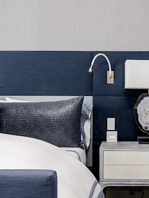 A modern bedroom features a bed with blue pillows, a stylish headboard, and a nightstand with a lamp and decorative items.