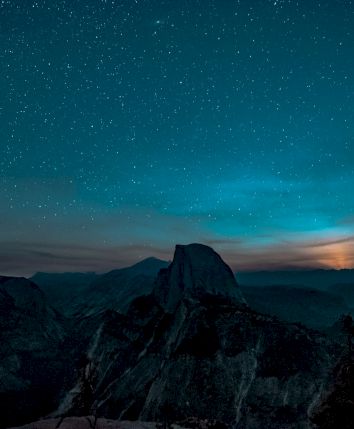A night sky filled with stars over a mountainous landscape, with a glowing horizon.