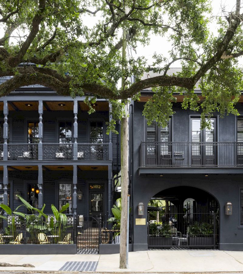 A two-story black building with balconies and a tree in front.