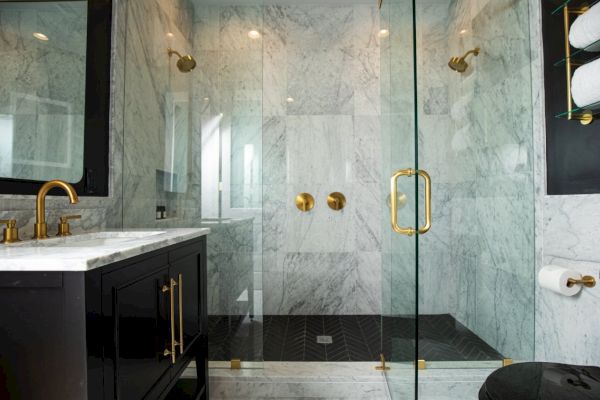 A modern bathroom features a glass shower with gold fixtures, black vanity, and marble surfaces, complemented by neatly stacked towels.