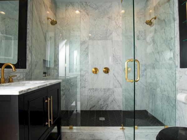 A modern bathroom features a glass shower with gold fixtures, black vanity, and marble surfaces, complemented by neatly stacked towels.