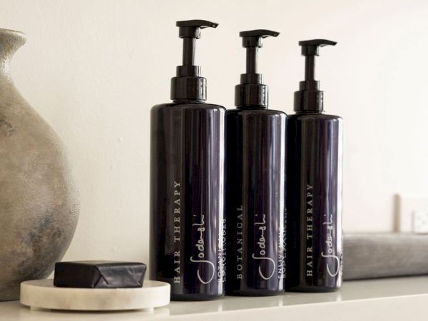 Three dark pump bottles labeled "Hair Therapy" and a small bar on a dish positioned on a shelf.