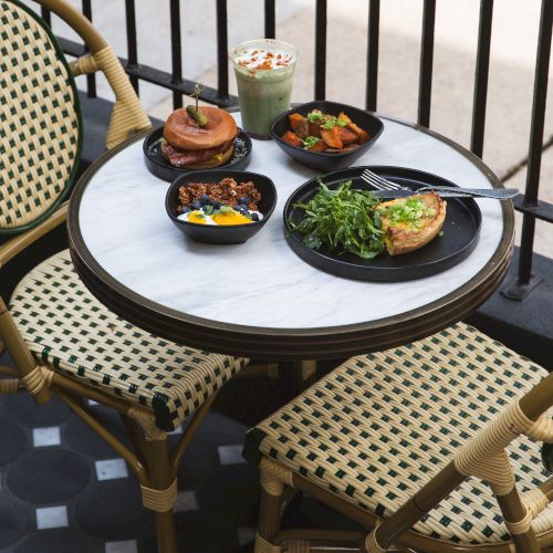 A caf&eacute; table set with a green smoothie, two small savory plates, dessert, and a side of fries with salad, outdoors by railings.