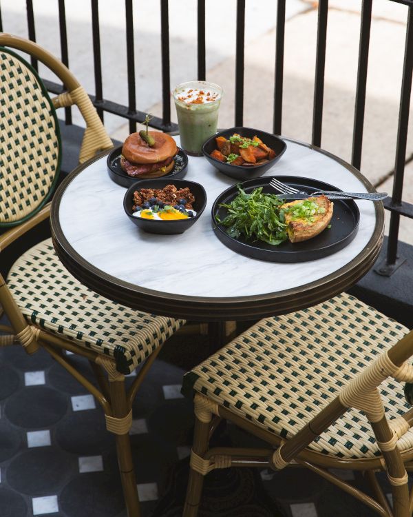 A caf&eacute; table set with a green smoothie, two small savory plates, dessert, and a side of fries with salad, outdoors by railings.