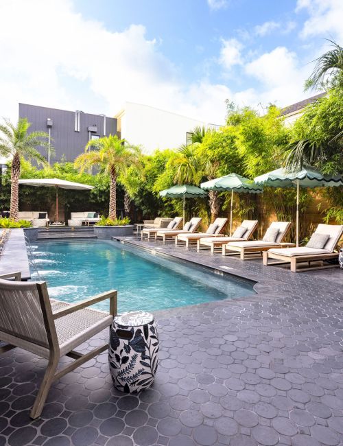 A serene pool area with lounge chairs, umbrellas, and lush greenery under a blue sky.