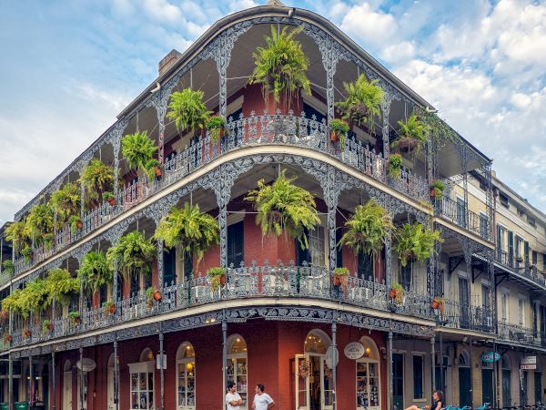 A historic building with ornate iron balconies and hanging plants on a street corner, likely in a Southern U.S. city.