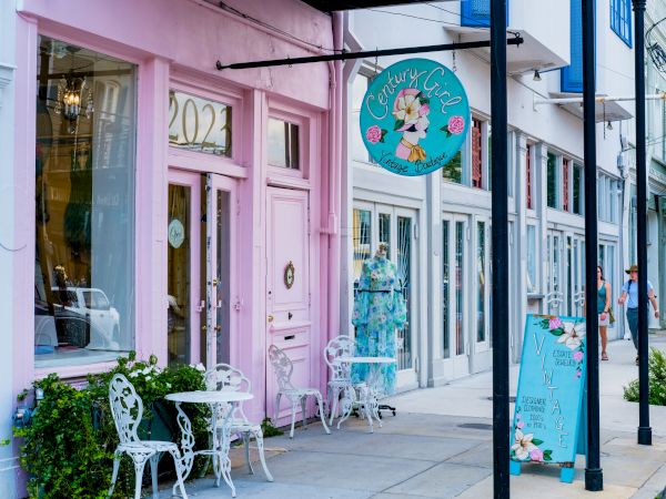 The image shows a pastel pink storefront with decorative tables and chairs outside, featuring a round sign that reads "Century Girl."