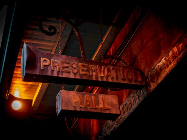 A sign reading "Preservation Hall" hangs from a building, illuminated by a nearby light.
