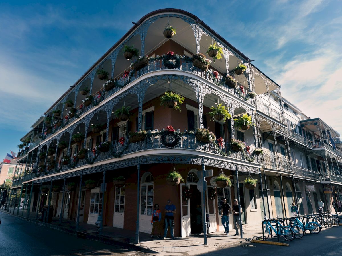 A historic building with wrought iron balconies and hanging plants, located at a street corner under a clear sky.