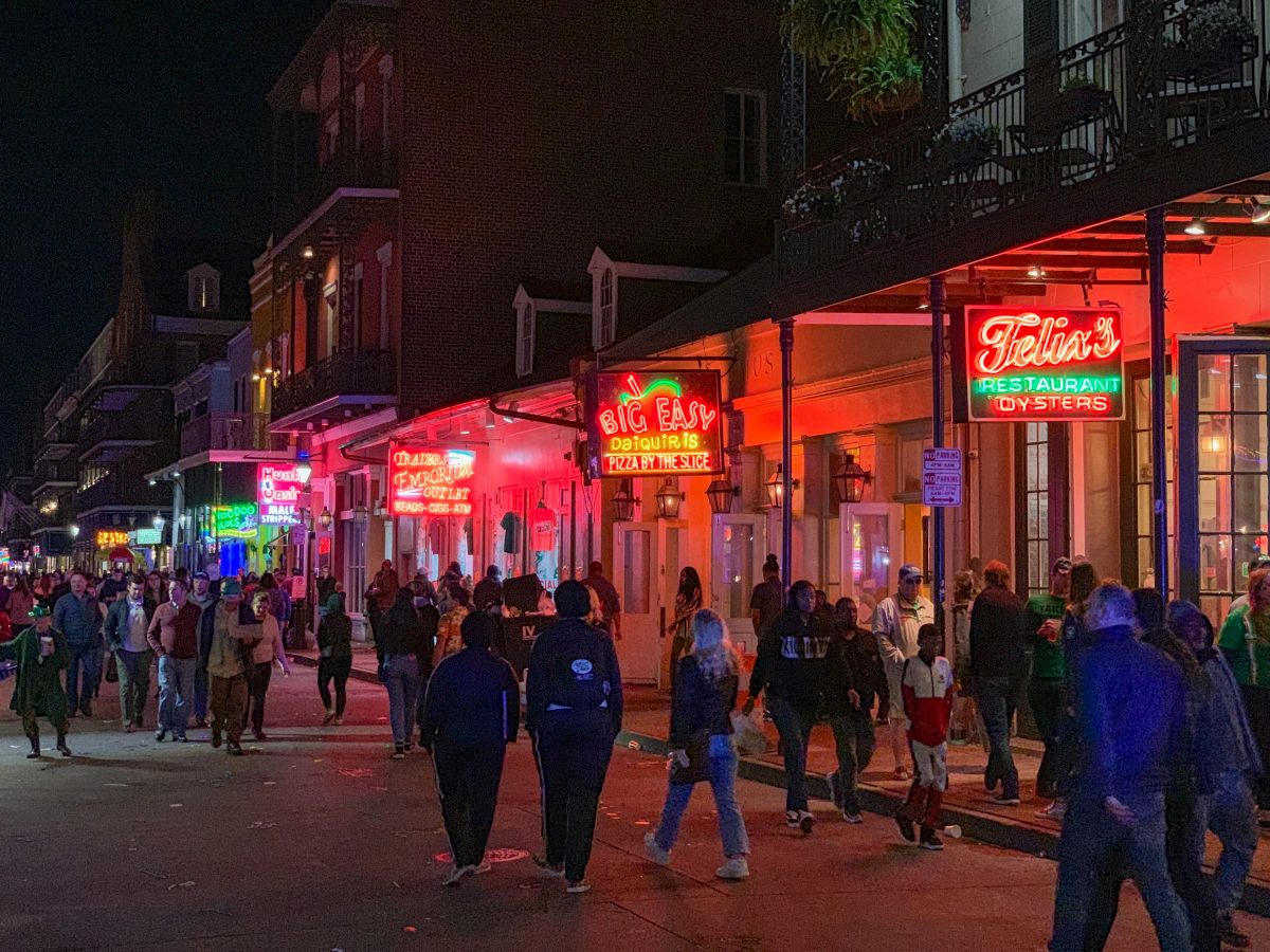 A bustling nighttime street scene with neon signs, including "Big Easy" and "Felix's Restaurant," and people walking along the sidewalk.