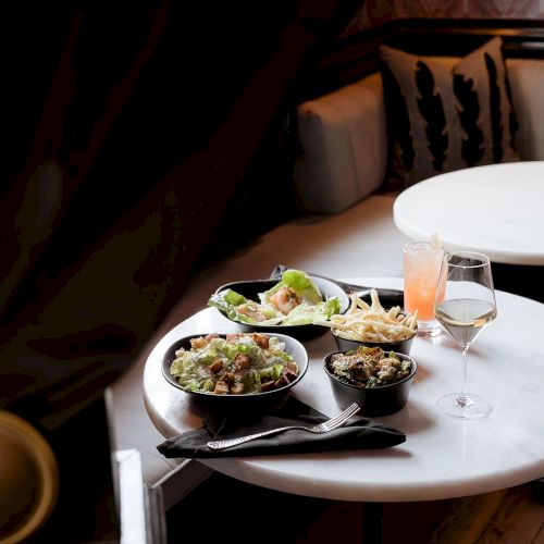 A round table with various dishes, including salad and fries, and drinks in a cozy restaurant setting.