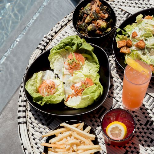 A poolside spread with lettuce wraps, fries, salad, broccoli, and two refreshing drinks, showcasing a delightful meal.