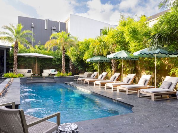 A modern backyard pool with lounge chairs, umbrellas, and lush greenery creates a relaxing outdoor space.