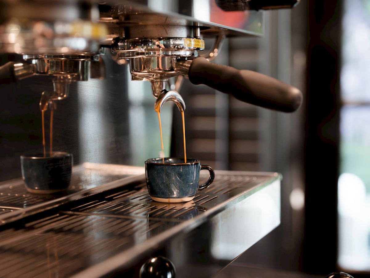 An espresso machine brewing coffee into small cups, with rich, dark coffee pouring from the spouts into the cup below on the tray.