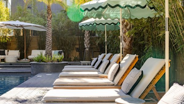 Poolside area with lounge chairs, green umbrellas, and palm trees. A relaxing outdoor setting.