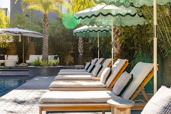 Poolside area with lounge chairs, green umbrellas, and palm trees. A relaxing outdoor setting.
