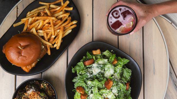 A table with a burger and fries, a Caesar salad, a drink, and a bowl of food.