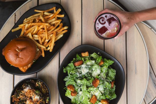 A table with a burger and fries, a Caesar salad, a drink, and a bowl of food.