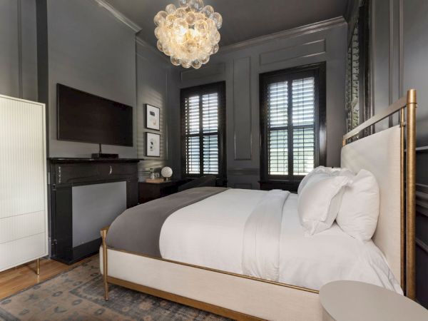A stylish bedroom with a double bed, modern chandelier, dark walls, large windows, and minimal decor, creating a cozy and elegant atmosphere.