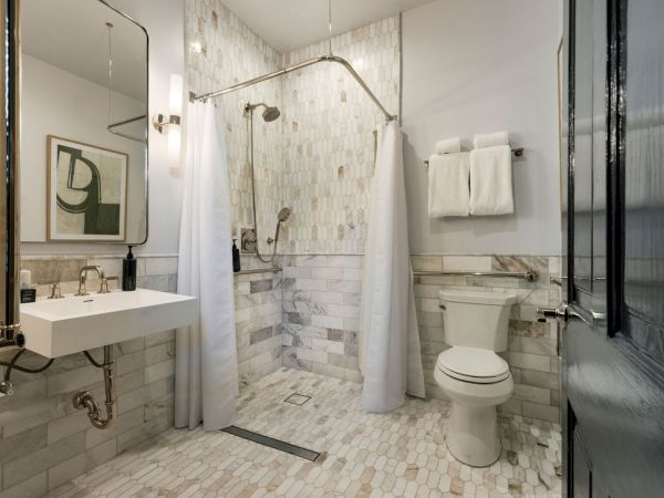 A modern bathroom with a walk-in shower, curtain, wall-mounted sink, toilet, towels, and a framed abstract artwork on the wall.