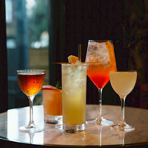 A variety of colorful cocktails on a round table, each in a different type of glass in a dimly lit setting.
