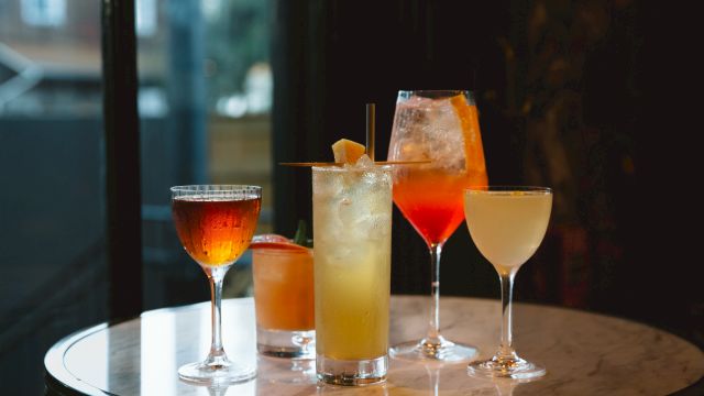 A variety of colorful cocktails on a round table, each in a different type of glass in a dimly lit setting.