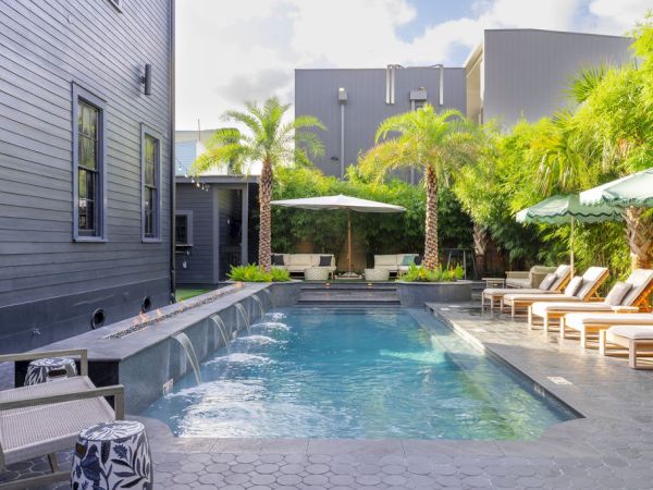 The image shows a modern backyard with a pool, lounge chairs, umbrellas, and palm trees, creating a relaxing outdoor space.