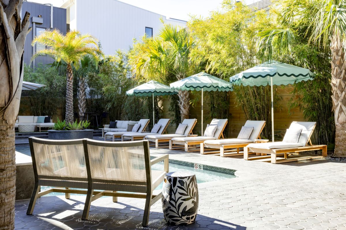 A poolside scene with chaise longues, parasols, and a pool surrounded by trees and greenery.