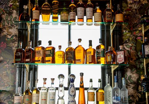 The image shows shelves filled with various bottles of liquor displayed against a decorative background.