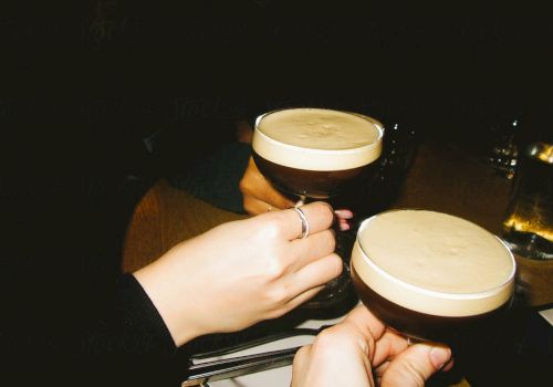 Two people clinking glasses filled with a creamy, frothy drink in a dimly lit setting.