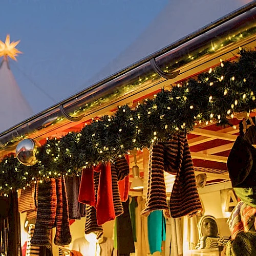A festive storefront with Christmas lights, garlands, and cozy sweaters hanging outside, topped by a glowing star on a snowy peak.