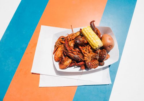 A plate of fried seafood and corn on the cob on a white napkin, set on a colorful striped surface.