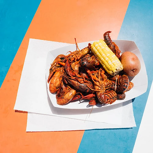 A plate of fried seafood and corn on the cob on a white napkin, set on a colorful striped surface.