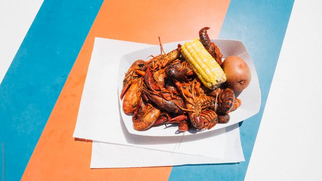 A plate of fried seafood and corn on the cob on a white napkin, set on a colorful striped surface.