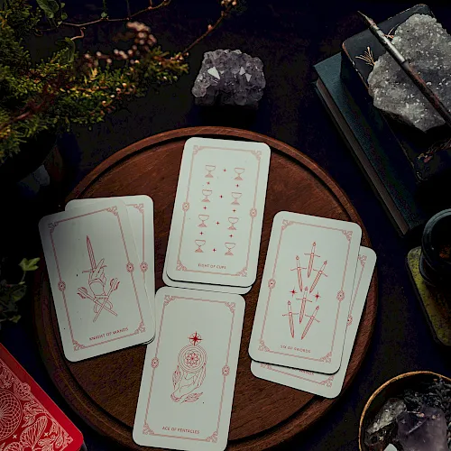 A tarot card spread on a wooden board with crystals, a wand, and candles&mdash;fortunes and mystic symbols in candlelit shadow.