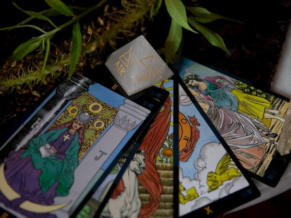 A spread of tarot-like cards with a central marker reading &ldquo;AIR&rdquo; and &ldquo;WATER,&rdquo; set on a leafy cloth.