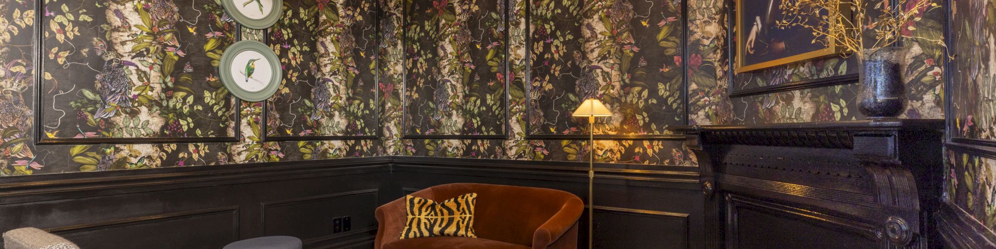 Cozy lounge with floral patterned room dividers, wall art, warm lamps, and a sofa and coffee table in the foreground.