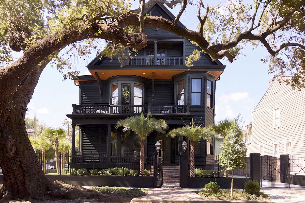 A three-story black house with balconies and a large tree in front.